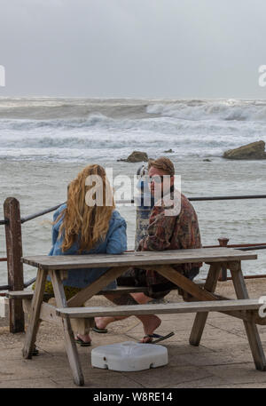 Un jeune couple assis sur un banc en regardant la mer sur un hivers rugueux et houleux jour sur l'île de Wight. Banque D'Images