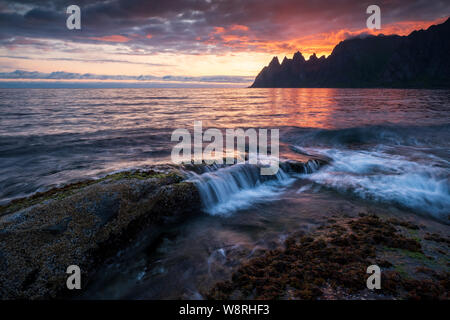 Plus d'écrasement des vagues rochers impressionnants oksen puissant avec des montagnes en arrière-plan à un coucher du soleil de minuit colorés, Tungeneset, Devils Jaw, Senja, norvégien Banque D'Images