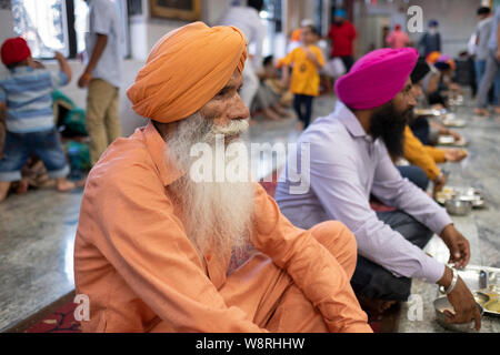 Un vieux homme sikh habillé en orange qui fait du bénévolat à une salle à manger commune (langar hall) dans un temple sikh dans South Ozone Park, Queens, New York. Banque D'Images