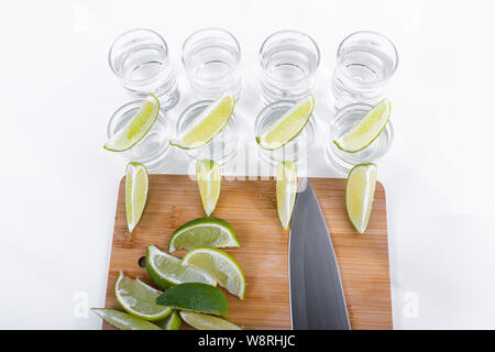 Tequila savoureux servi dans huit coups avec des tranches de citron vert à côté d'une planche à découper en bois avec un couteau et des tranches de citron vert sur le dessus - Vue de dessus Banque D'Images