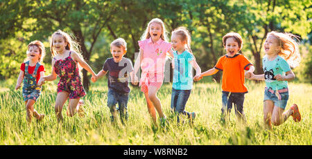 Grand groupe d'enfants, amis, garçons et filles courir dans le parc aux beaux jours d'été dans des vêtements décontractés . Banque D'Images