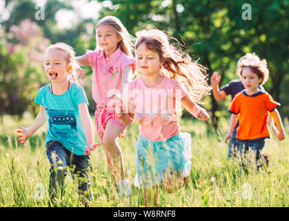 Grand groupe d'enfants, amis, garçons et filles courir dans le parc aux beaux jours d'été dans des vêtements décontractés . Banque D'Images