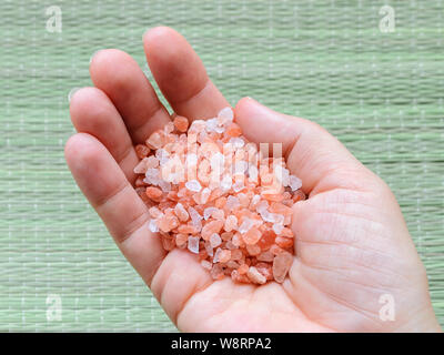 Femme main tenant les cristaux de sel de l'himalaya rose sur tapis vert. Sel de l'Himalaya est utilisé en cuisine, en médecine et en cosmétologie. Vue d'en haut. Banque D'Images