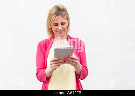 Portrait de beaux succès businesswoman jeune femme en blouse rose, à l'aide de commandes et de lecture message intéressant sur sa tablette avec heureux fac Banque D'Images