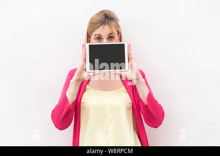 Portrait de surpris belle jeune femme en blouse rose debout et tenant tablet écran vide , couvrant la bouche et looking at camera with big eye Banque D'Images