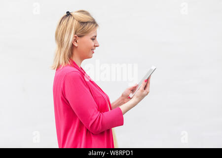 Vue de côté portrait de femme d'affaires réussie jeune femme en blouse rose, à l'aide de commandes et de lecture message intéressant sur sa tablette avec heureux fac Banque D'Images