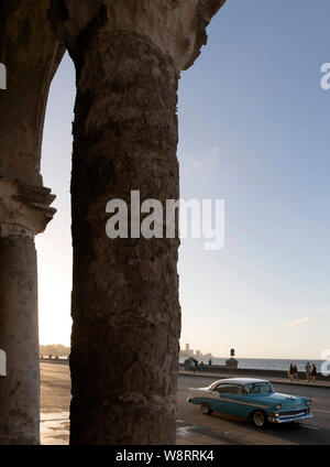 Voir entre colonnes surmonté d'un bâtiment ancien sur le Malecon la rue la plus célèbre de La Havane Cuba, montrant la mer, vieilles voitures et à Vedado Banque D'Images