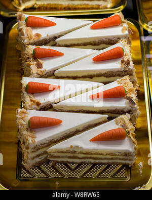 Gâteau aux carottes avec décoration en massepain en forme de carotte. Pièces triangulaires de gâteau avec une couche de biscuits et crème blanche sur un showc confiserie Banque D'Images