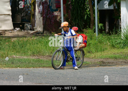 Deux petits vietnamiens boy riding bike aller à l'école à midi, élève en uniforme circuler à bicyclette et s'arrêter au bord de la route de l'autoroute, Vietnam Banque D'Images