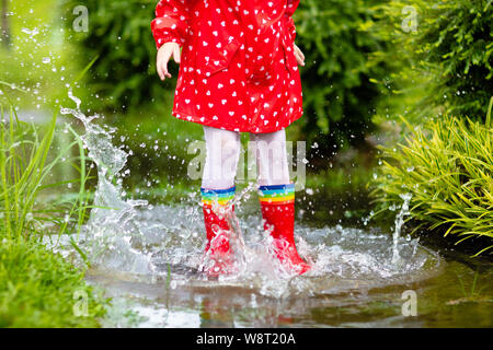 Kid jouer sous la pluie en automne parc. Le saut de l'enfant dans la boue flaque sur l'automne des pluies 24. Petite fille dans des bottes de pluie et veste rouge à l'extérieur par temps sh Banque D'Images