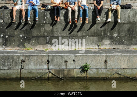 Plusieurs jeunes hommes sont assis sur le mur de l'rivedside et profiter de la pause pendant la journée ensoleillée. Banque D'Images