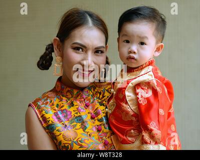 Habillée femme chinoise thaïlandaise tient son petit garçon dans ses bras, pendant le Nouvel An chinois, et déclinée pour l'appareil photo. Banque D'Images