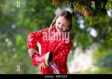 Avec des bottes en caoutchouc pour enfants jouant dans la pluie en automne parc. Enfant en flaque boueuse par temps pluvieux jour d'automne. Botte de ville pleine d'eau. Petite fille en veste rouge Banque D'Images