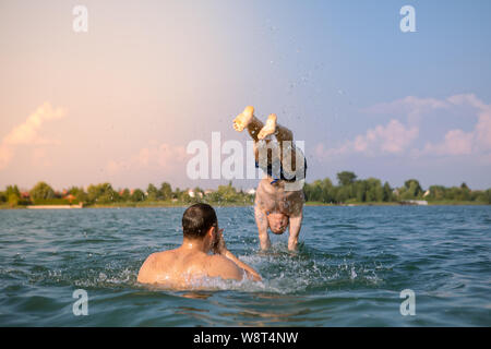 Couple d'amis mâles s'amusant dans le lac en tenant l'appareil photo sur l'action selfies sautant d'épaules Banque D'Images