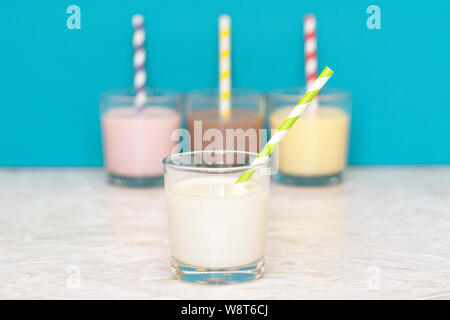Le lait frais avec une paille papier rétro en face d'une rangée de milkshakes contre un arrière-plan bleu sarcelle Banque D'Images