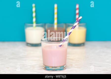 Lait frappé aux fraises avec une paille papier rétro en face d'une rangée de lait frais et aromatisé de lait frappé contre un arrière-plan bleu sarcelle Banque D'Images