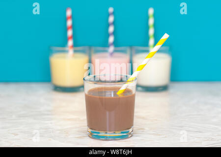 Milkshake au chocolat avec une paille papier rétro en face d'une rangée de milkshakes et lait frais contre un arrière-plan bleu sarcelle Banque D'Images