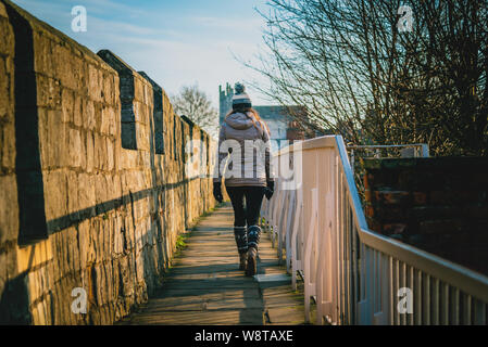 Vue arrière de la silhouette d'une jeune femme marchant le long des murs de la ville de York sur une journée ensoleillée. Banque D'Images