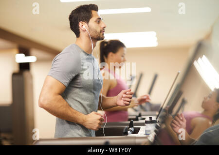 Vue latérale du Moyen-Orient portrait of handsome man running sur tapis roulant dans une salle de sport et d'écouter de la musique, copy space Banque D'Images