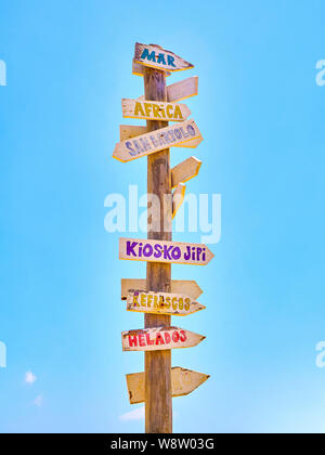 Grand poster avec panneaux en bois couleur pointant vers des destinations diverses et une plage services en espagnol sur un ciel bleu. L'Afrique, de la mer, San Bartolo, Hip Banque D'Images