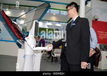 Un employé chinois serre la main d'un robot au cours du 16ème Salon chinois des technologies dans la ville de Shenzhen, province du Guangdong en Chine du sud, le 16 novembre 2014. Banque D'Images