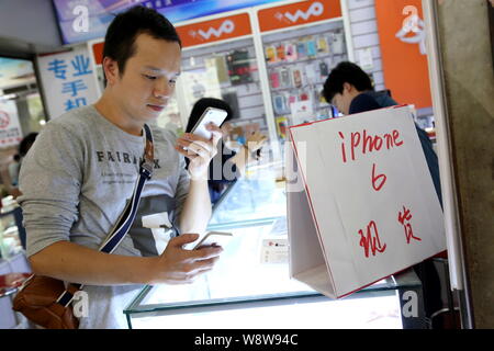 --FILE--un client chinois essaie l'un l'iPhone d'Apple 4s à côté de smartphone une publicité pour l'iPhone 6 smartphone à un téléphone portable du marché de Shanghai, C Banque D'Images