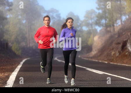 Fonctionnement sain runner homme et femme d'entraînement sur route de montagne. Le jogging homme et femme modèle de remise en forme hors de la formation pour le marathon sur route forestière en nature paysage incroyable. Deux coureurs execising Banque D'Images