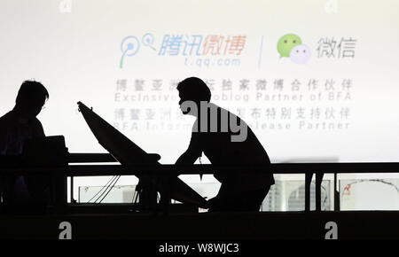 --FILE--Employés sont vus en face d'une publicité pour t.qq.com et la messagerie mobile app Weixin, ou de Tencent WeChat, pendant le Forum de Boao pour l Banque D'Images