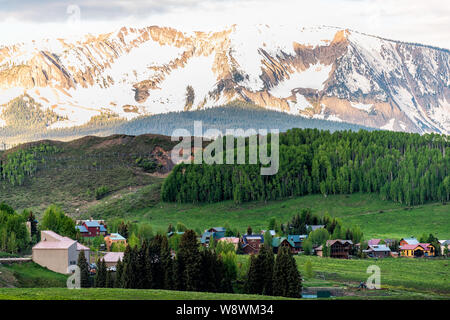Mount Crested Butte, Colorado village en été avec des maisons en bois par le lever du soleil sur les collines avec des arbres verts Banque D'Images