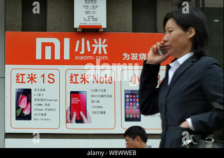 --FILE--un piéton parle sur son téléphone portable alors qu'elle passe devant une publicité pour les smartphones Xiaomi à Yichang City, Hubei Chines centrale provinc Banque D'Images