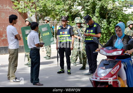 --FILE--Local résidents Ouïgours chinois passent par des agents de police et paramilitaires des policiers qui montent la garde dans les rues de Kashgar, dans les Chines Xinj Banque D'Images