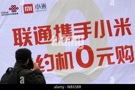 --FILE--un piéton parle sur son téléphone mobile devant une publicité pour China Unicom et Xiaomi à Beijing, Chine, 10 avril 2013. Xiaomi Inc., Chi Banque D'Images