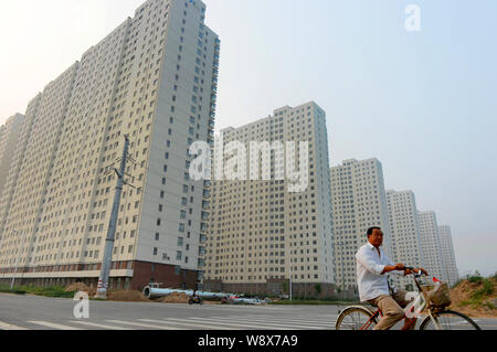 Un homme chinois cours des cycles, nouvellement construit appartement résidentiel bâtiments dans la ville de Puyang, province du Henan Chine centrale, 3 août 2014. La croissance dans Banque D'Images