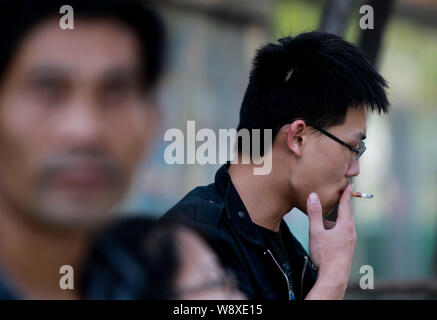 --FILE--Un homme fume une cigarette qu'il attend à un arrêt d'autobus dans la ville de Qingdao, province du Shandong, Chine de l'Est 30 mai 2013. Chine Continentale auth santé Banque D'Images