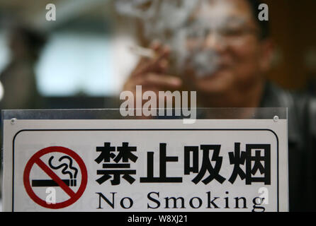 --FILE--un Chinois fume une cigarette près de l'affiche non- fumeurs à Xuzhou, Jiangsu province de Chine orientale, le 25 novembre 2014. La Chine est considerin Banque D'Images