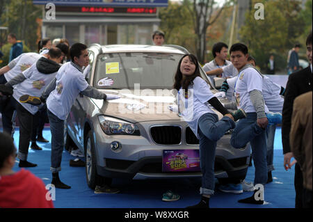 Les concurrents chinois garder leurs mains sur une BMW X1 SUV tout en se tenant sur un seul pied pendant une main-sur-voiture endurance à un campus en ville Shap Banque D'Images