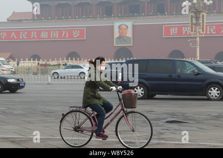 --FILE--un cycliste portant un masque de visage rides sur la ChangAn Avenue, près de la place Tiananmen en gros le smog à Pékin, Chine, 14 avril 2014. Le gouvernement Banque D'Images