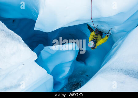 Dans l'homme jecket jaune une section escalade en surplomb de glace dans un moulin glacier en Alaska. Flagging son pied comme son outil brise la glace en petits Banque D'Images