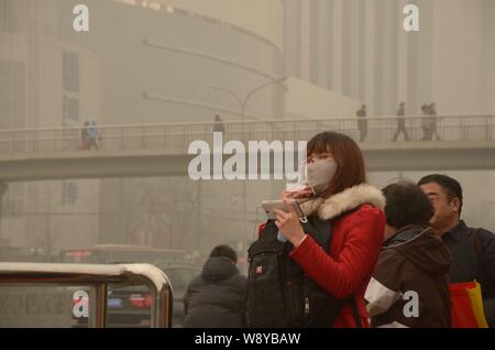 --FILE--passagers chinois, certains d'entre eux porter des masques, d'attente à un arrêt de bus dans le smog lourde à Beijing, Chine, 26 février 2014. Un assureur chinois ha Banque D'Images