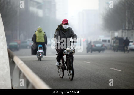 --FILE--un cycliste portant un masque de visage rides sur une route dans le smog lourde à Tianjin, Chine, 7 décembre 2013. Les gouvernements de Pékin, Tianjin et Hebe Banque D'Images