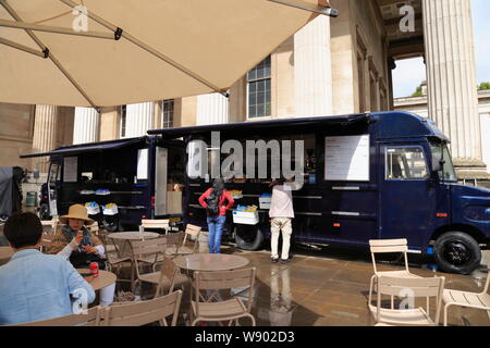 Les gens s'asseoir sous un parasol à un café en plein air, tandis que d'autres achètent des rafraîchissements dans un camion alimentaire au British Museum de Londres, Royaume-Uni. Banque D'Images