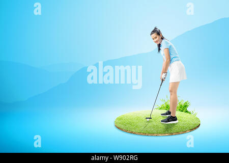 Femme Asiatique avec un putter golf club prêt à frapper la balle sur le green golf course Banque D'Images