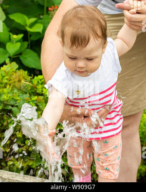 Petite fille jouant avec des jets d'eau dans une fontaine. Un enfant sur une promenade dans le parc joue avec de l'eau, le bébé monte dans la fontaine Portrait d'une ch Banque D'Images