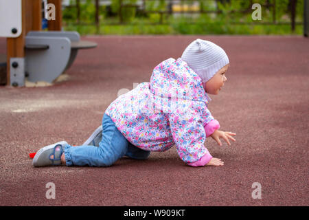 Baby Girl en se déplaçant sur le terrain de jeu. Un enfant dans des vêtements chauds à quatre pattes. Un bébé de 1 an marche près de la maison de printemps automne vêtements. Ensemble de la chi Banque D'Images