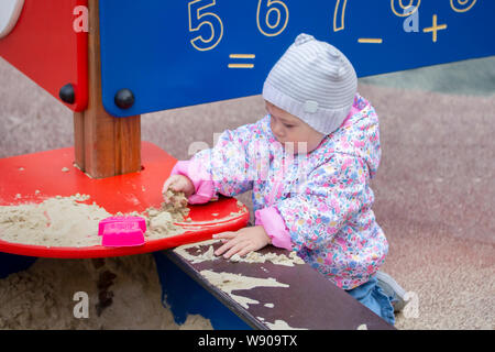 Bébé fille jouant avec le sable. Une fille dans une rose et un chapeau pour une promenade joue avec du sable dans un bac à sable, ramasse le sable, le monde autour d'études. Un petit Banque D'Images