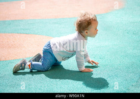 Un bébé de 1 an se traîne autour de l'aire pour une promenade. Le gamin est vêtue de jeans, pulls et bottes denim. Banque D'Images