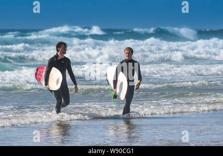 Surfers mâles sortant de la mer avec leurs planches à Newquay dans Fistral à Cornwall. Banque D'Images