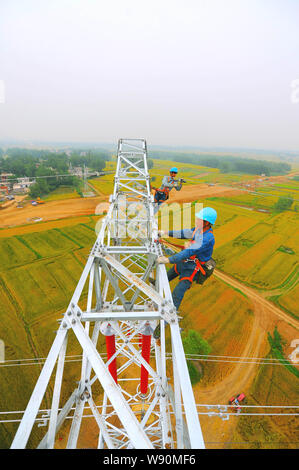 Les travailleurs chinois monter les câbles haute tension sur un pylône de plus de champs dans Lujiagang massive village, ville, comté de Fengyang Xiangzhou District, Foshan City, est de la Chine Banque D'Images