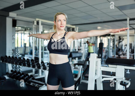 Femme dans la salle de sport l'échauffement avant l'exercice les bras tendus Banque D'Images