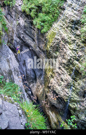 Fille de traverser un pont de bois suspendu à la gorge de Postalm via ferrata, l'Autriche, avec l'eau et forme une petite cascade sur les parois du canyon. Pers verticale Banque D'Images